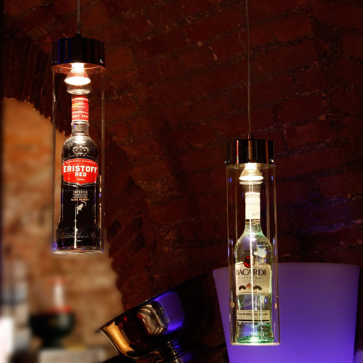 Deux suspensions cylindriques en verre renfermant des bouteilles d'alcool sur fond de mur de briques.
