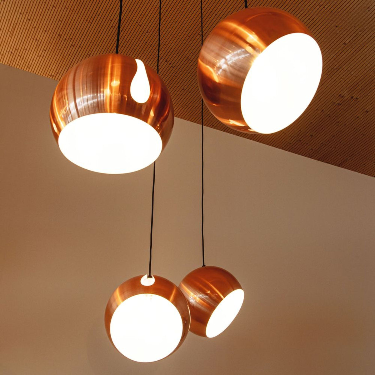 Vue en contre-plongee de globes cuivres allumes sous un plafond en lattes de bois