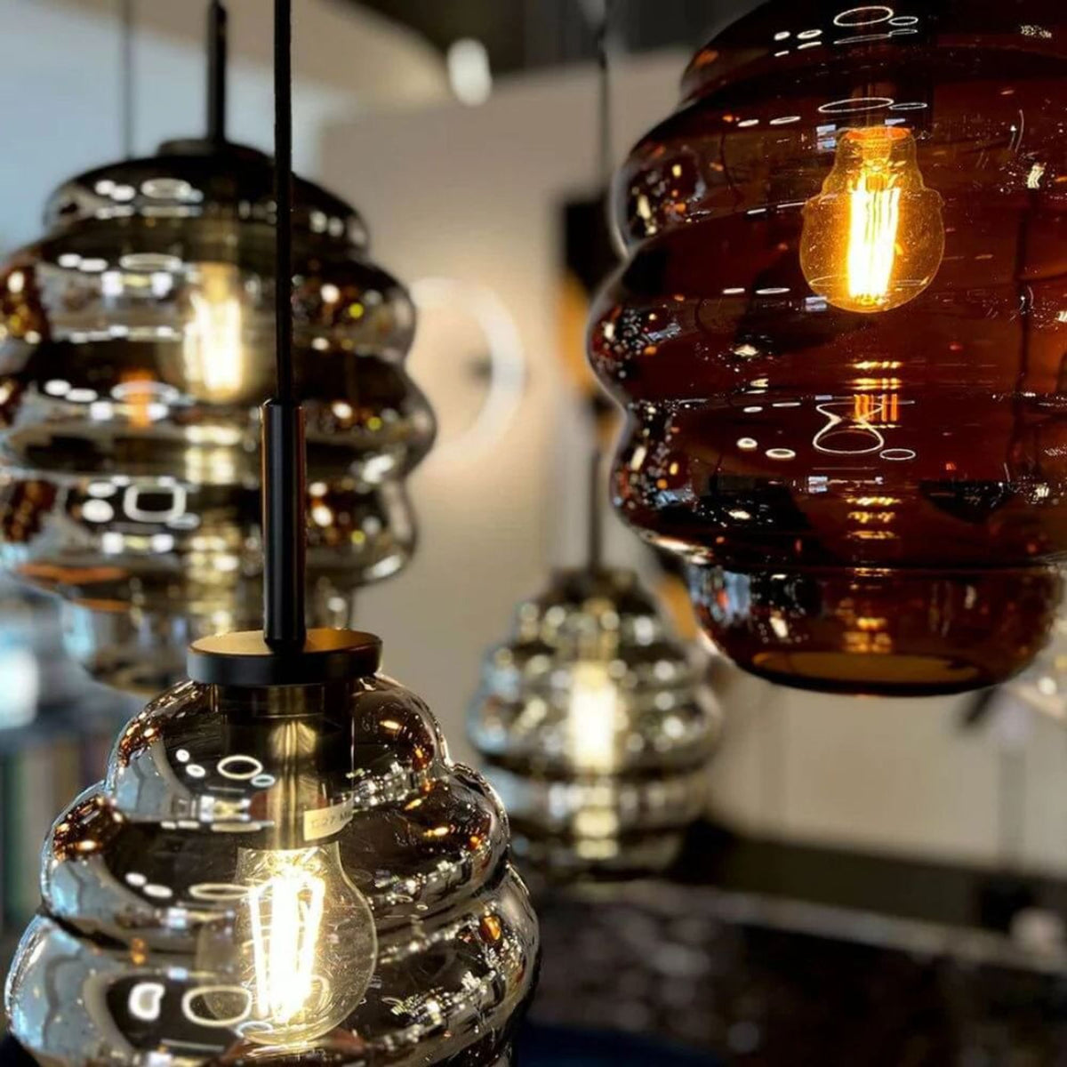 Gros plan en showroom sur plusieurs verres striés ambrés et fumés suspendus à tiges noires.