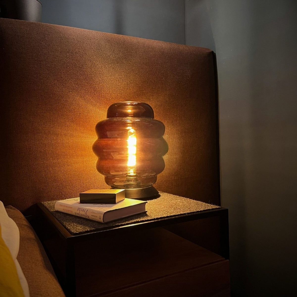 Lampe ambrée allumée sur table de nuit, livres posés à côté, ambiance chaleureuse