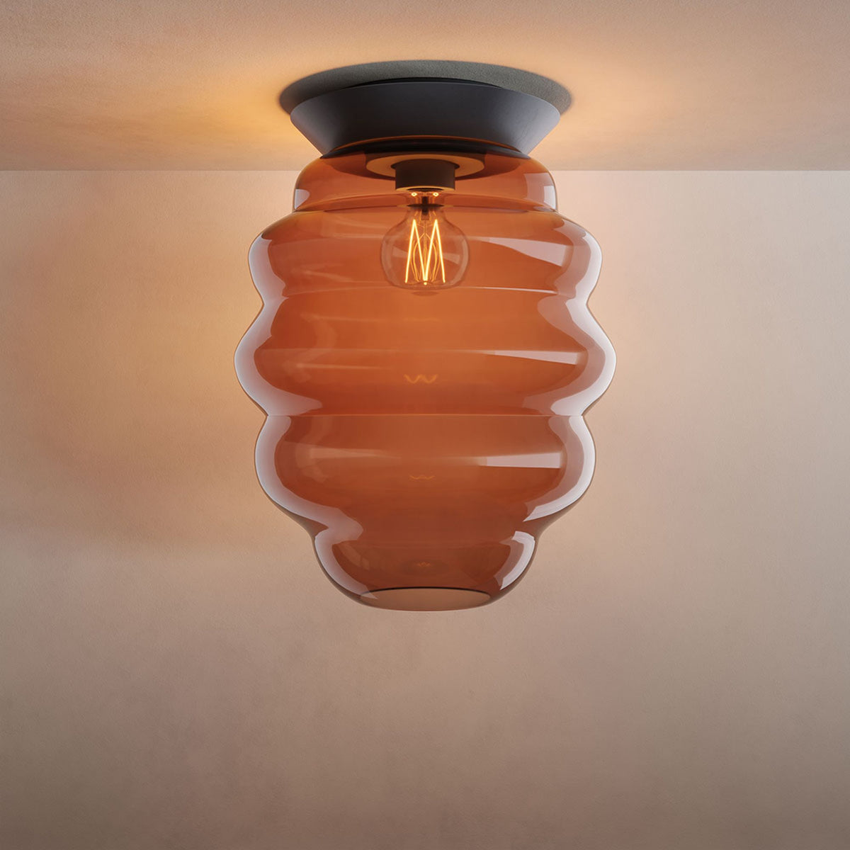 Même plafonnier en verre ambré orangé, de face sur fond beige uniforme.