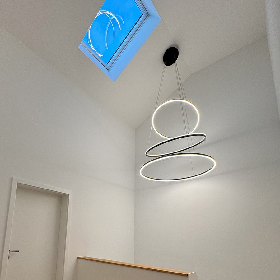 Suspension allumée dans un hall blanc avec fenêtre de toit, vue de profil