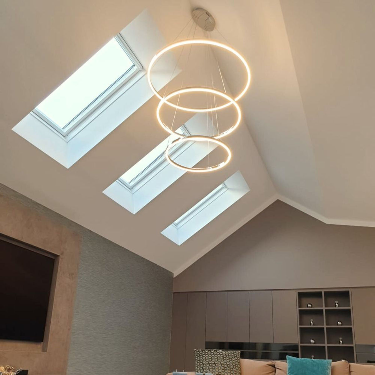 Trois anneaux lumineux suspendus sous des fenêtres de toit dans un salon