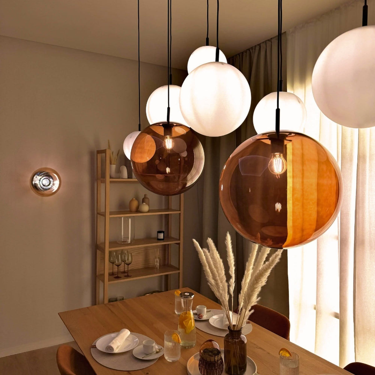 Ambiance salle à manger avec plusieurs globes ambrés et blancs suspendus au-dessus de la table.