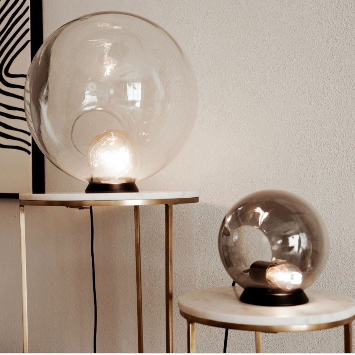 Deux lampes globe de tailles différentes posées sur guéridons en marbre