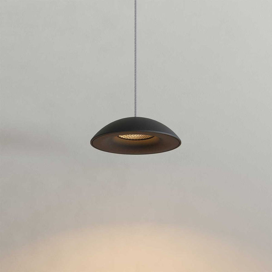 Gros plan sur un luminaire noir suspendu, montrant la coupole et le réflecteur interne éclairé.