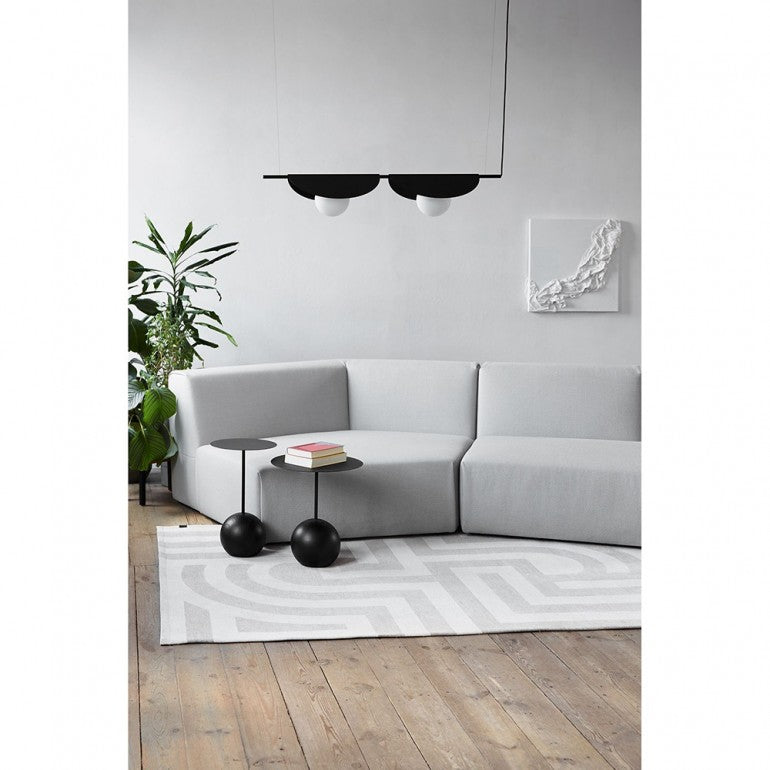 Mise en ambiance du luminaire noir suspendu au-dessus d'un canapé gris et d'un tapis.