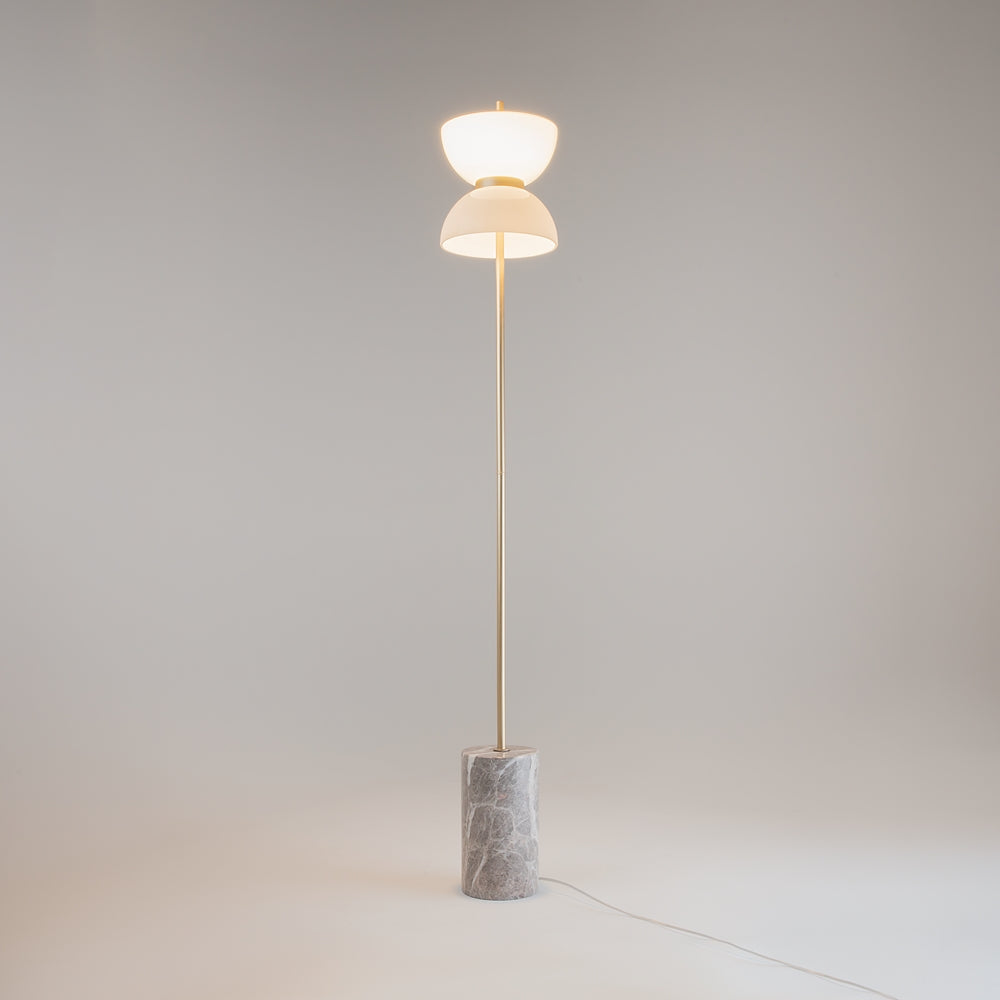 Lampadaire allumé dans une pièce neutre, double abat-jour blanc diffusant une lumière chaude.