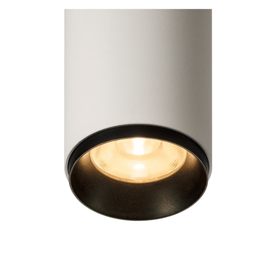 Gros plan du bas du luminaire allumé, bord noir et ampoule chaude visible.
