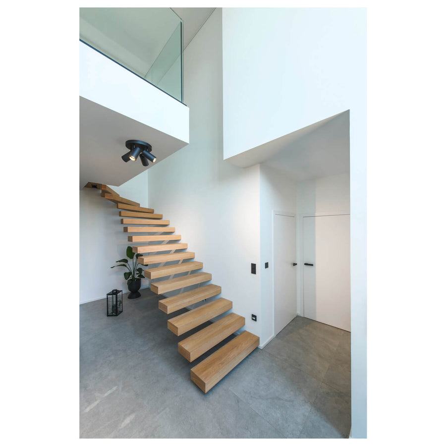 Le spot à quatre têtes noires installé au plafond d'une entrée moderne avec escalier.