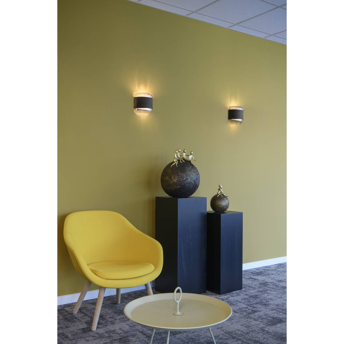 Salon contemporain avec fauteuil jaune et deux appliques murales sur un mur olive