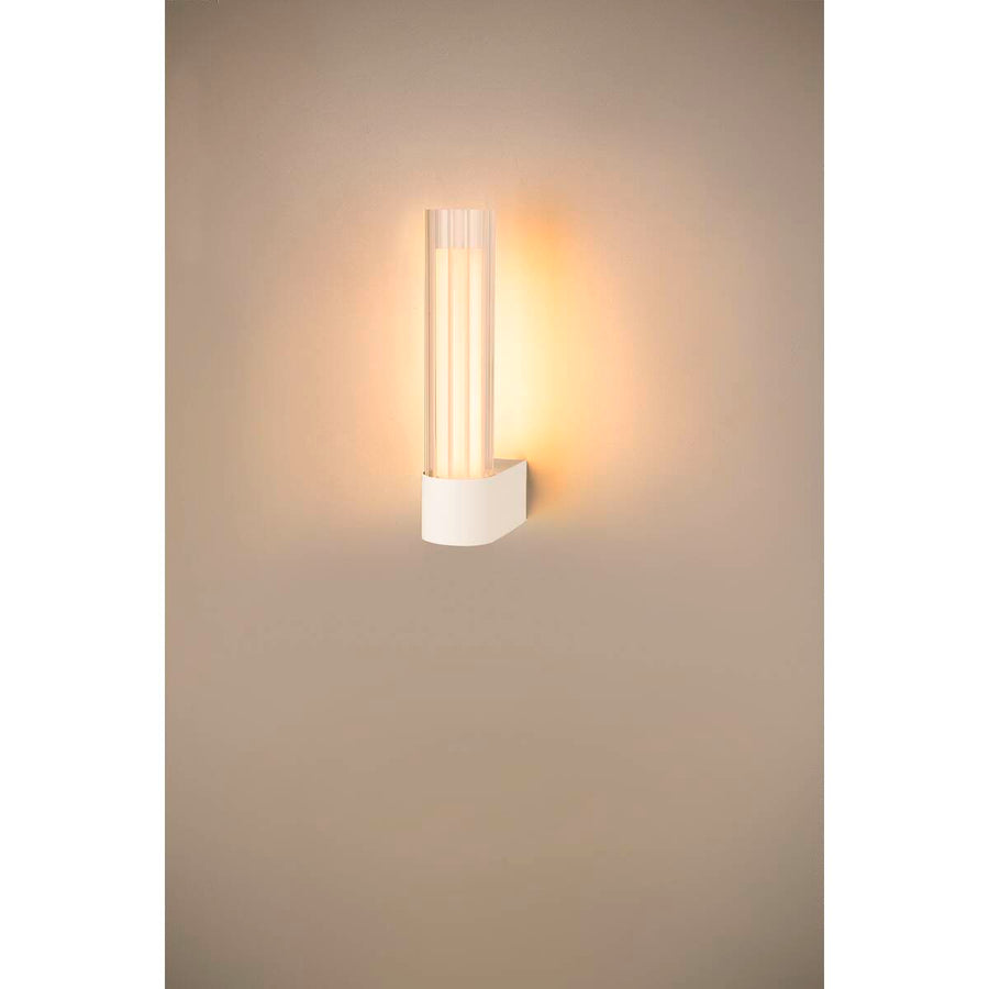Applique allumée fixée au mur, halo chaud projeté sur la paroi beige.