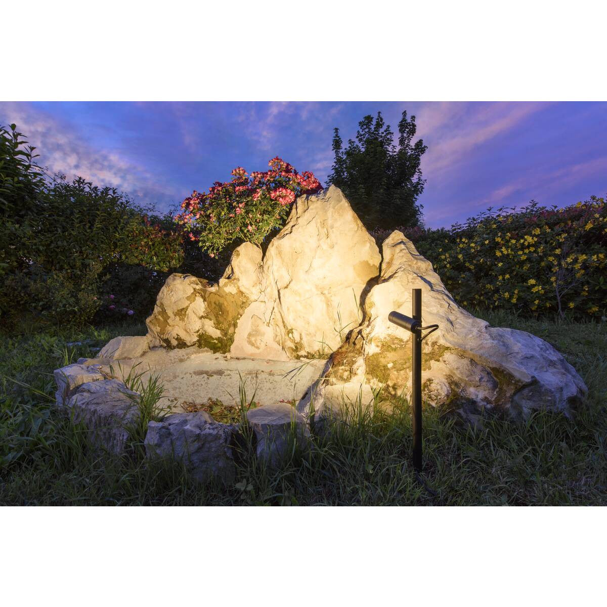 Mise en ambiance nocturne dans un jardin, le spot éclaire un rocher et des fleurs.