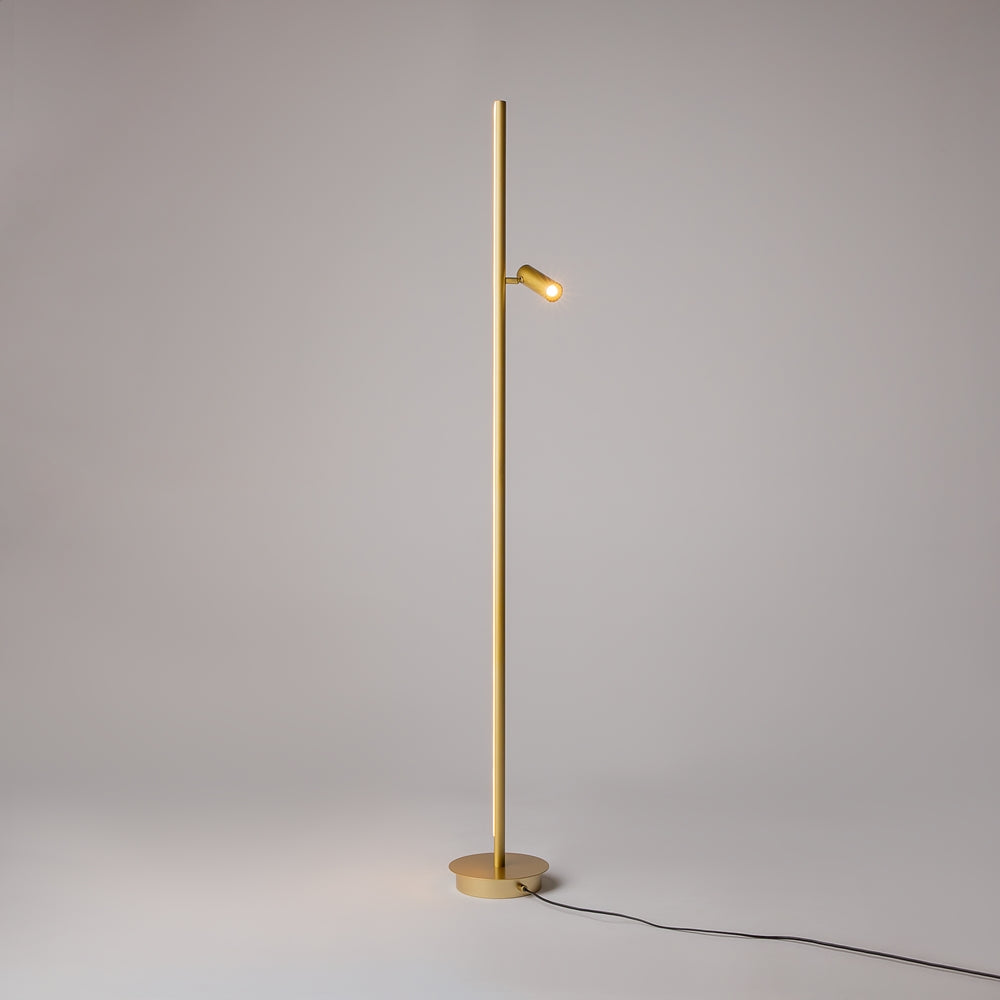 Lampadaire allumé dans un studio gris, petit spot doré éclairant vers la droite.