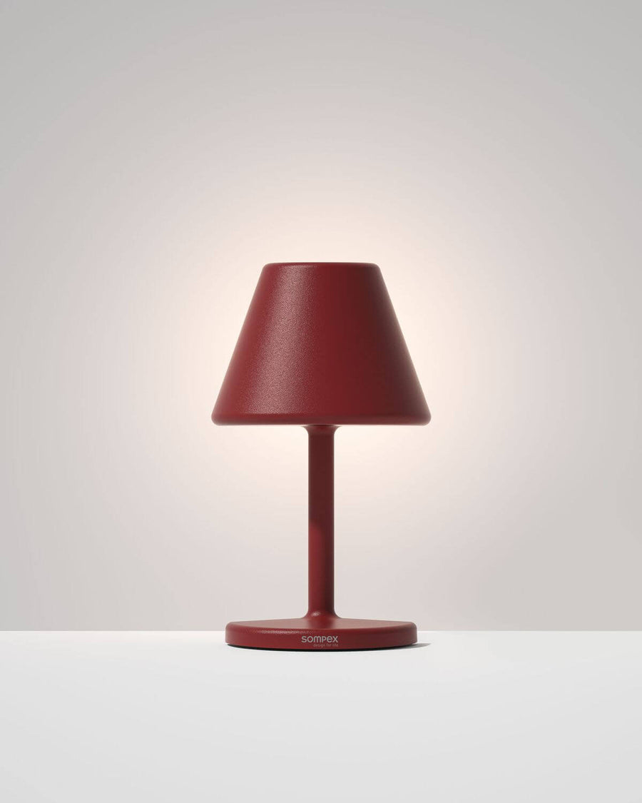 Luminaire rouge allumé sur fond clair, détail de la finition granulée et du socle.