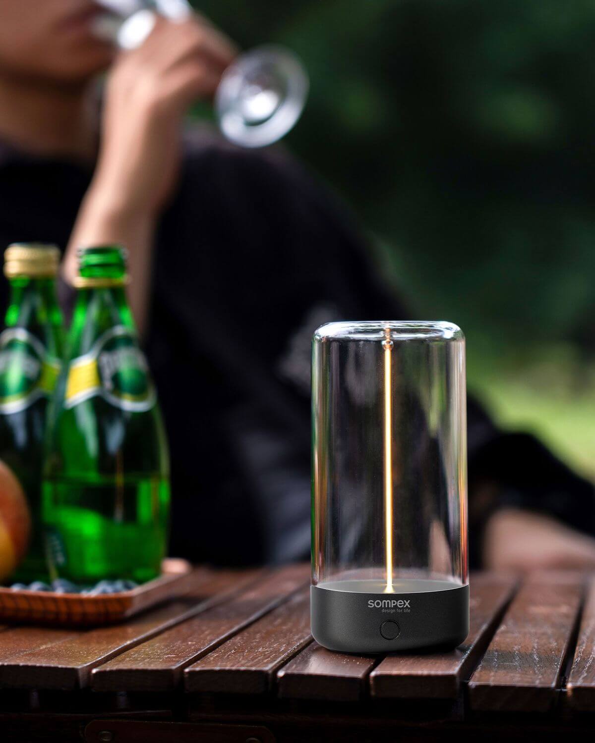 Mise en ambiance extérieure sur table en bois, lampe allumée près de bouteilles