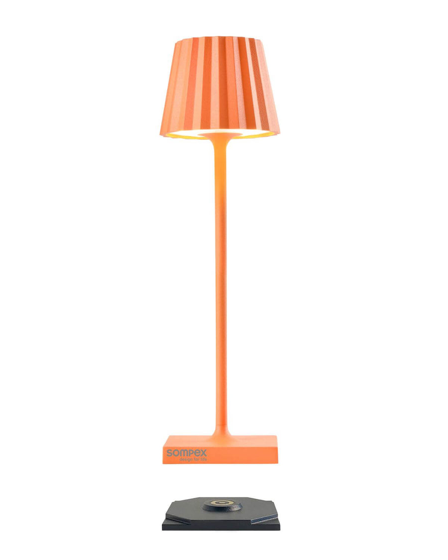 Vue de la lampe orange et de son socle de recharge noir à contact central