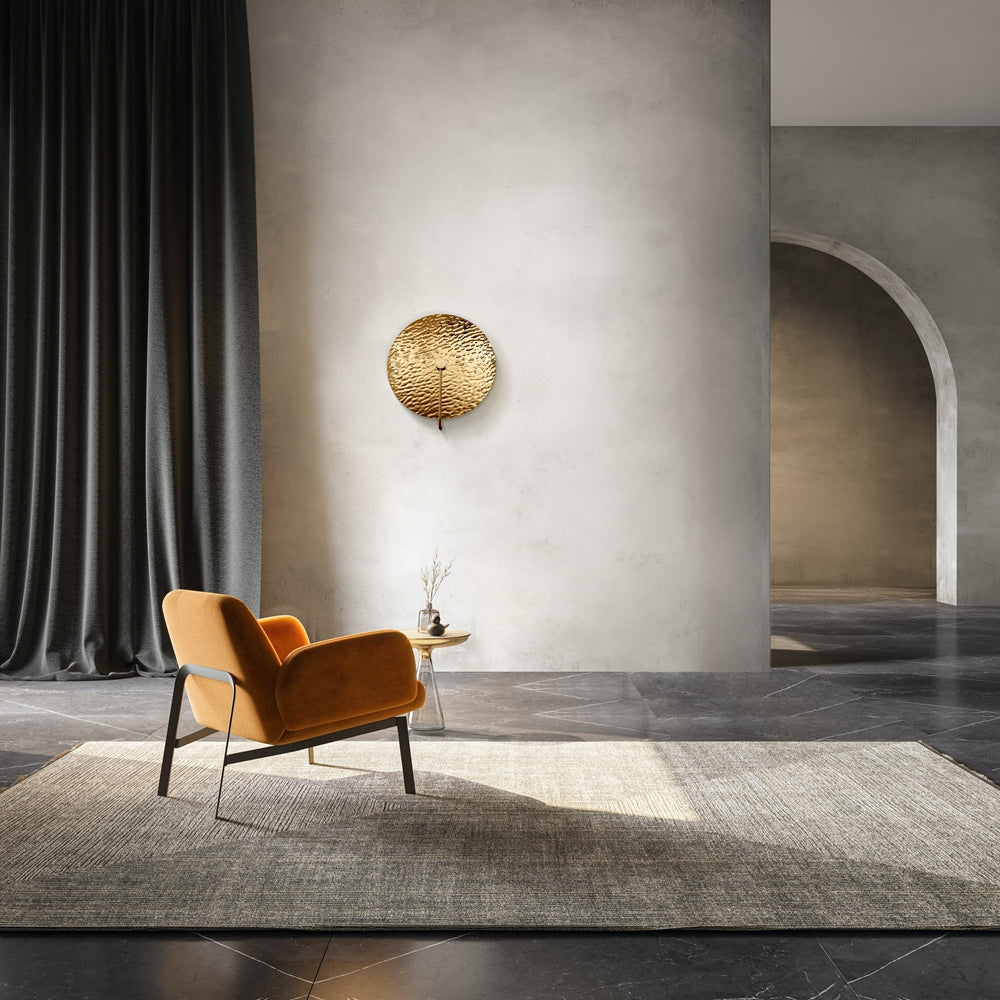 Mise en ambiance salon : applique dorée fixée sur mur béton, fauteuil orange et tapis