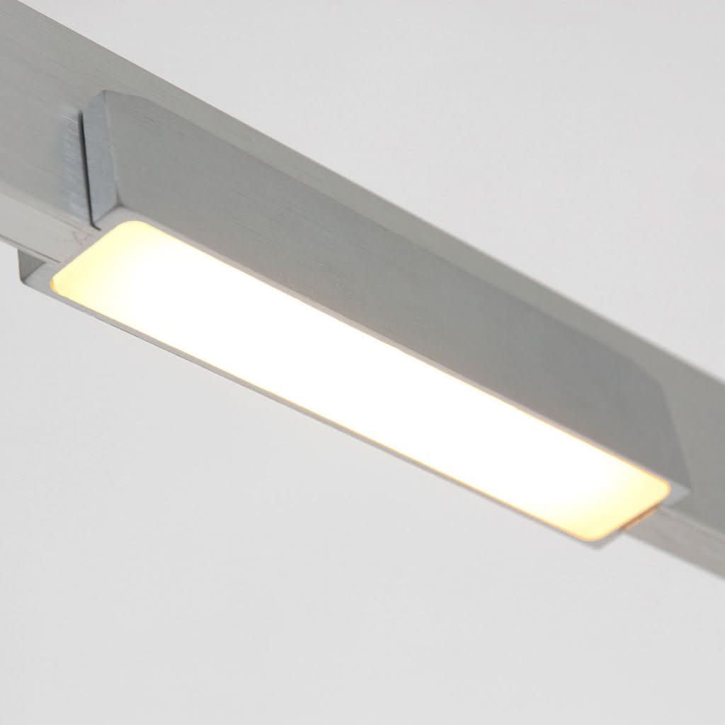 Gros plan sur le diffuseur rectangulaire éclairé et le support métallique du luminaire.