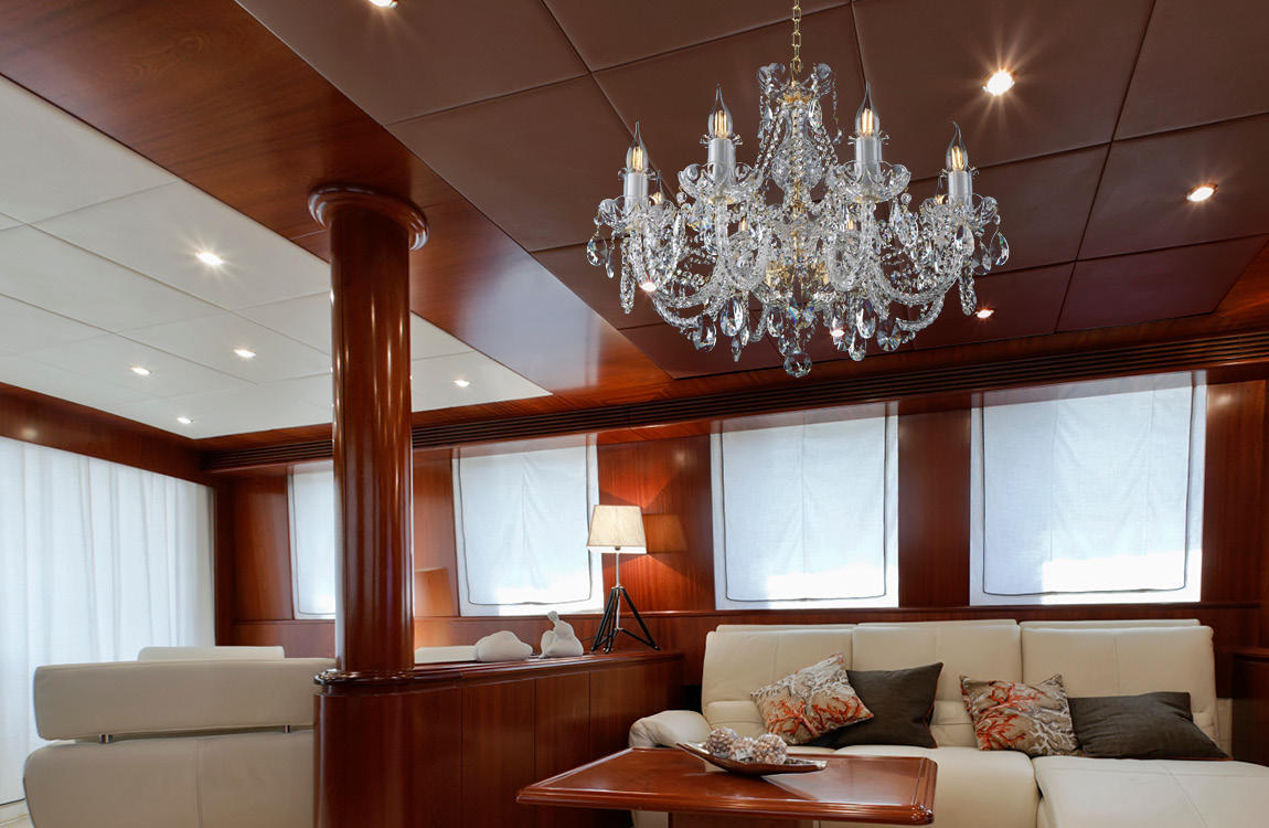 Lustre installé au plafond d'un salon de yacht, boiseries sombres et canapé crème