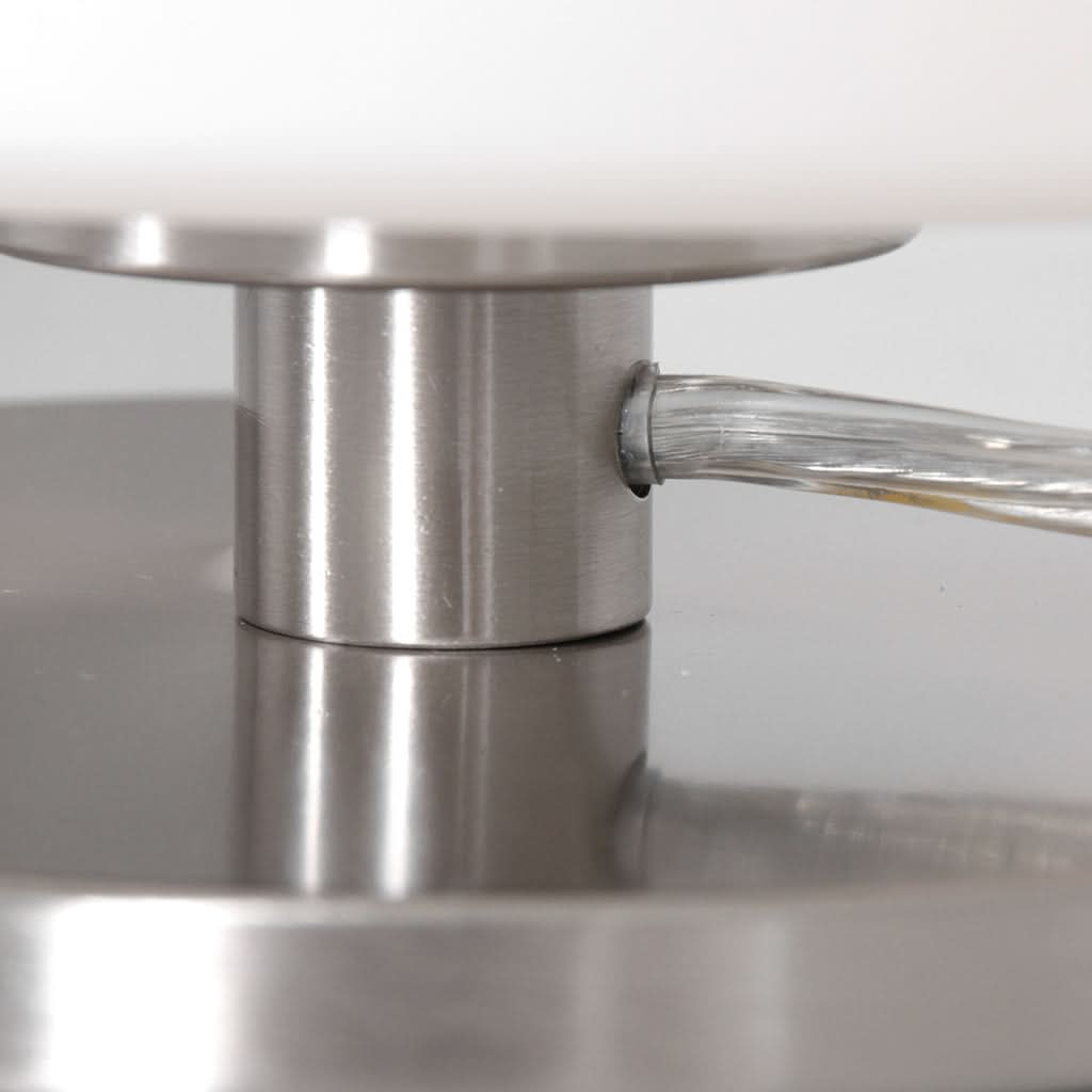 Très gros plan sur l'entrée du câble transparent dans le pied cylindrique en acier brossé.