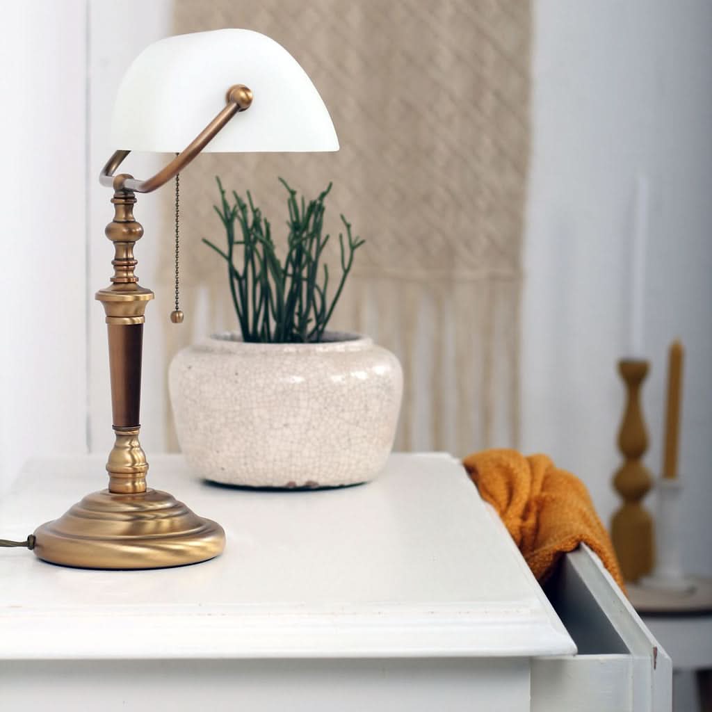 Lampe posée sur une commode blanche, à côté d'une plante en pot et d'une serviette.