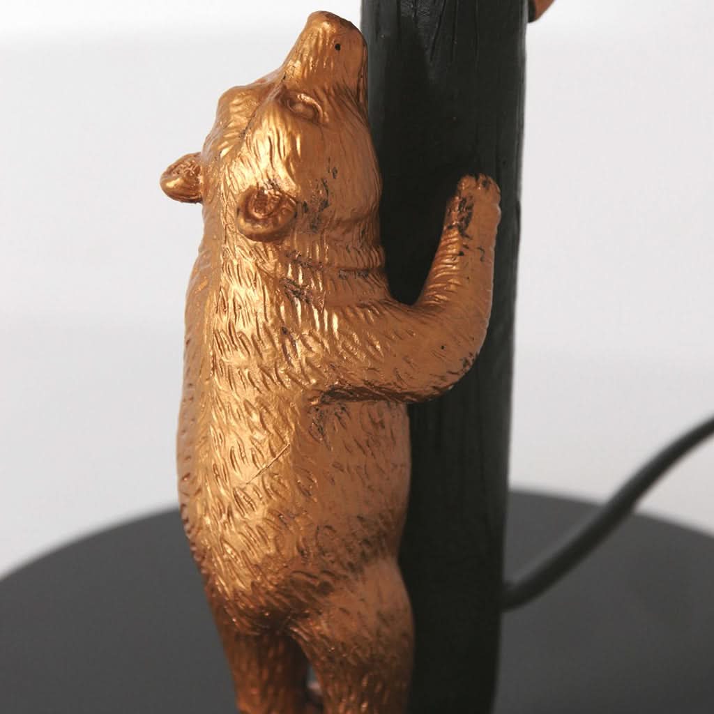 Détail du petit ours doré grimpant sur le fût noir texturé