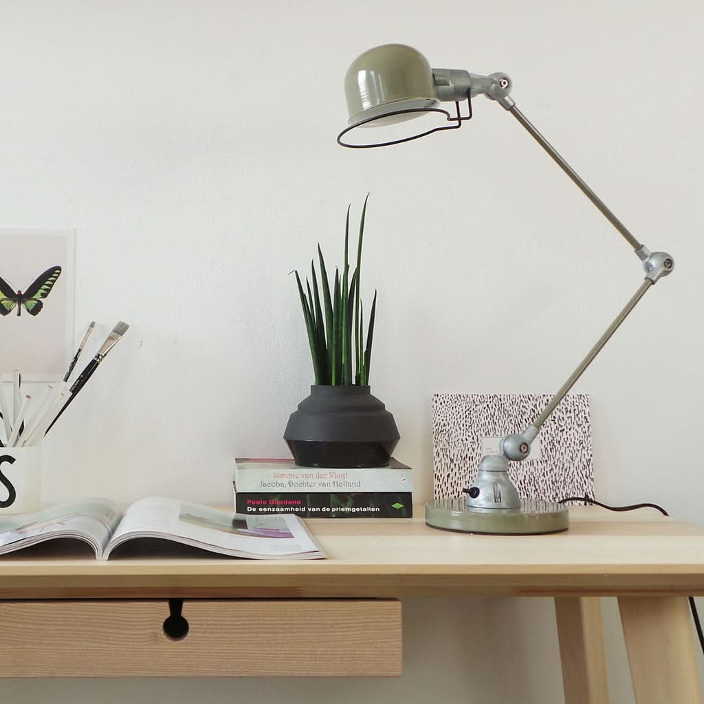 Lampe posée sur un bureau en bois près de livres, plante et cartes.