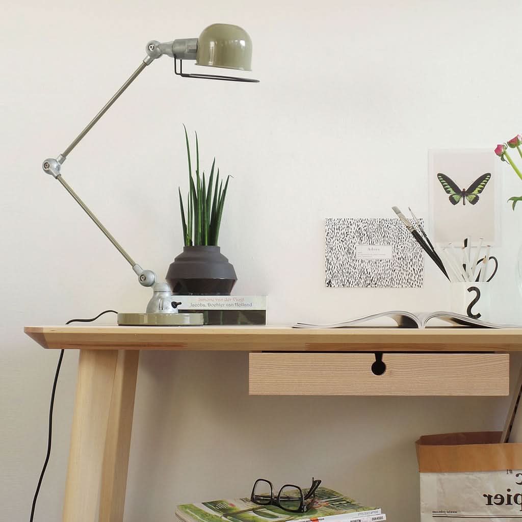 Lampe de bureau en métal vert installée sur une table en bois clair.