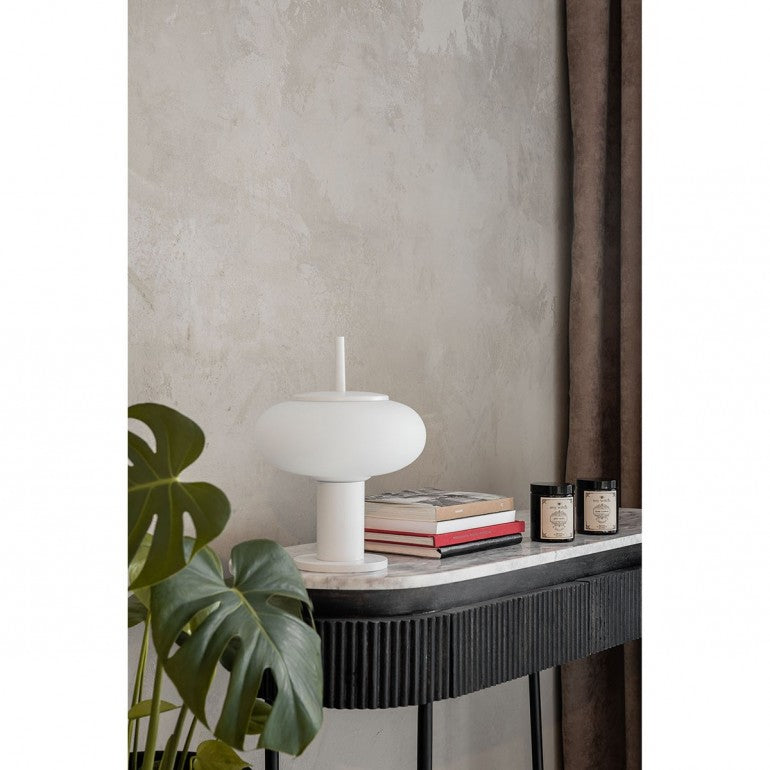 Mise en ambiance sur console en marbre, à côté de livres, bougies et plante verte.