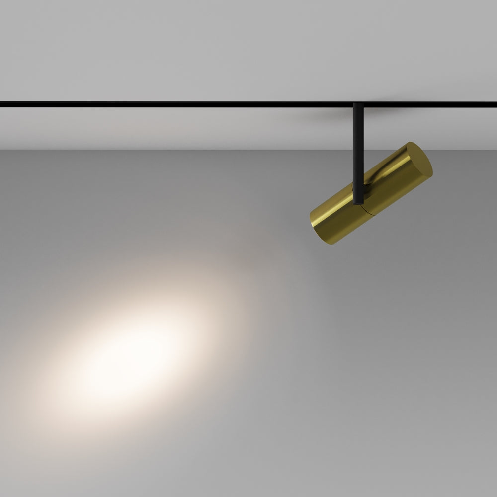 Mise en ambiance : faisceau lumineux diffusé sur un mur gris, spot doré incliné.