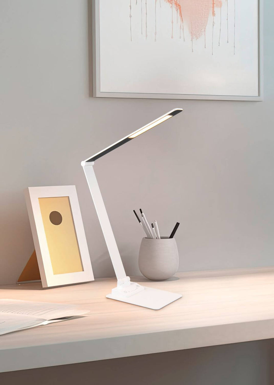 Vue rapprochée de la lampe blanche allumée, posée sur un bureau en bois clair.