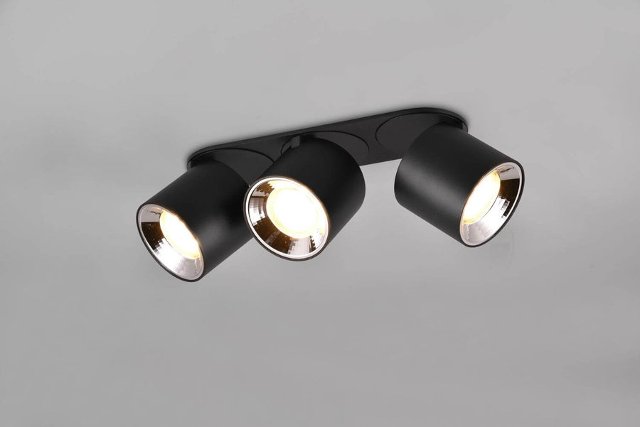 Vue de trois quarts du plafonnier noir à spots cylindriques orientables, éclairage allumé.