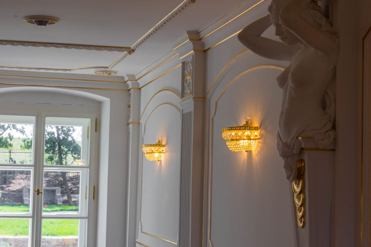 Mise en ambiance : deux appliques allumées sur boiseries blanches et moulures dorées