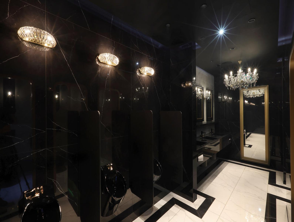 Mise en ambiance : trois appliques murales allumées sur marbre noir d'un toilette luxueux