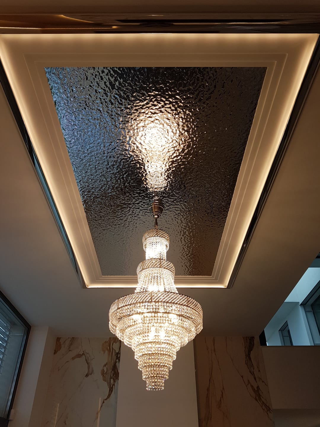 Vue du dessous montrant le reflet du lustre sur un plafond en verre texturé
