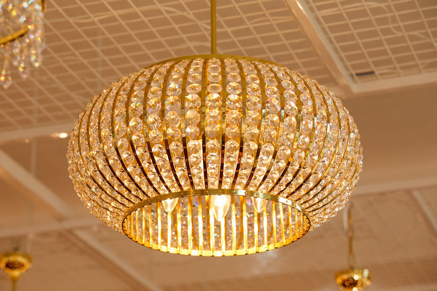 Vue de dessous du plafonnier allumé, montrant la structure dorée et les ampoules fixées au plafond.