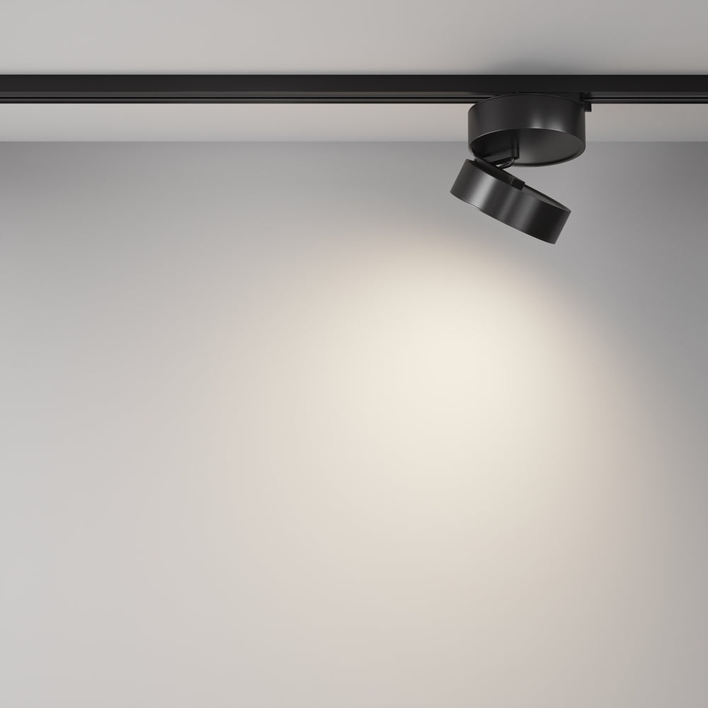 Spot incliné éclairant un mur blanc, installé sur un rail au plafond