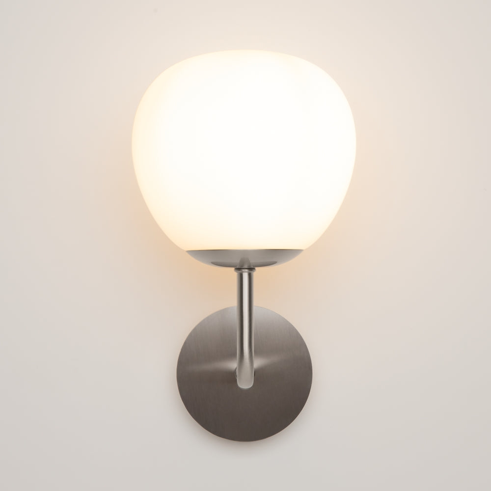 Vue de face du luminaire allumé, bras métallique coudé et platine ronde