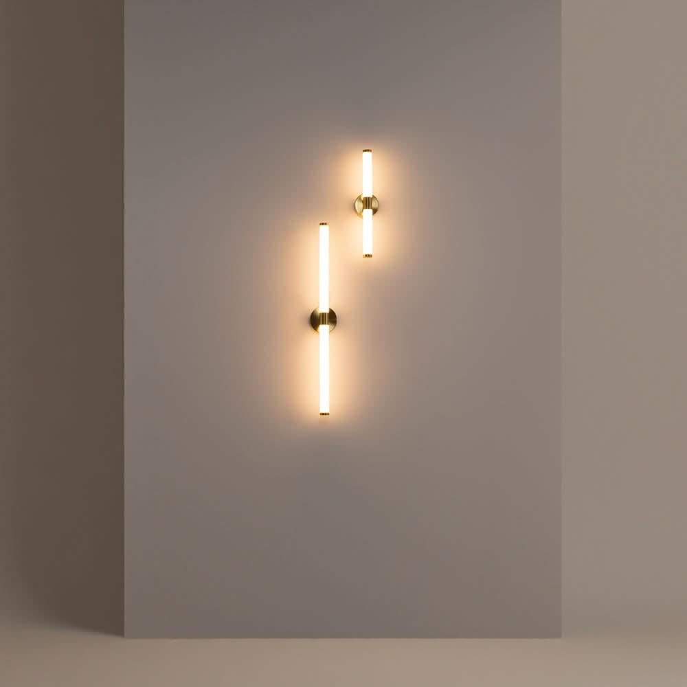 Deux appliques tubulaires dorées allumées, décalées, sur mur gris