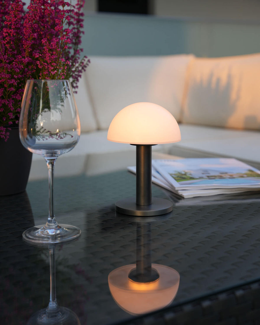 Lampe posée sur table basse en verre, reflet, verre de vin et coussins clairs