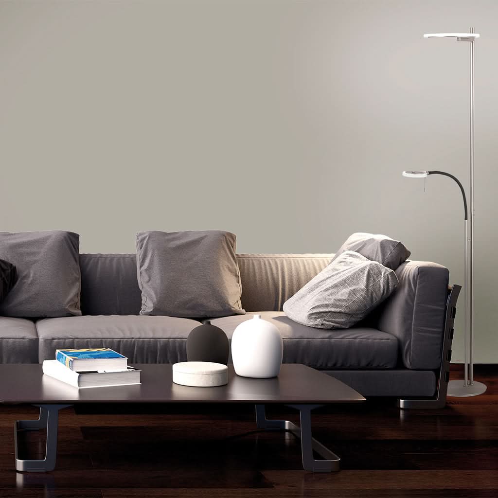 Mise en ambiance salon moderne, lampe de sol allumée près d'un canapé gris.