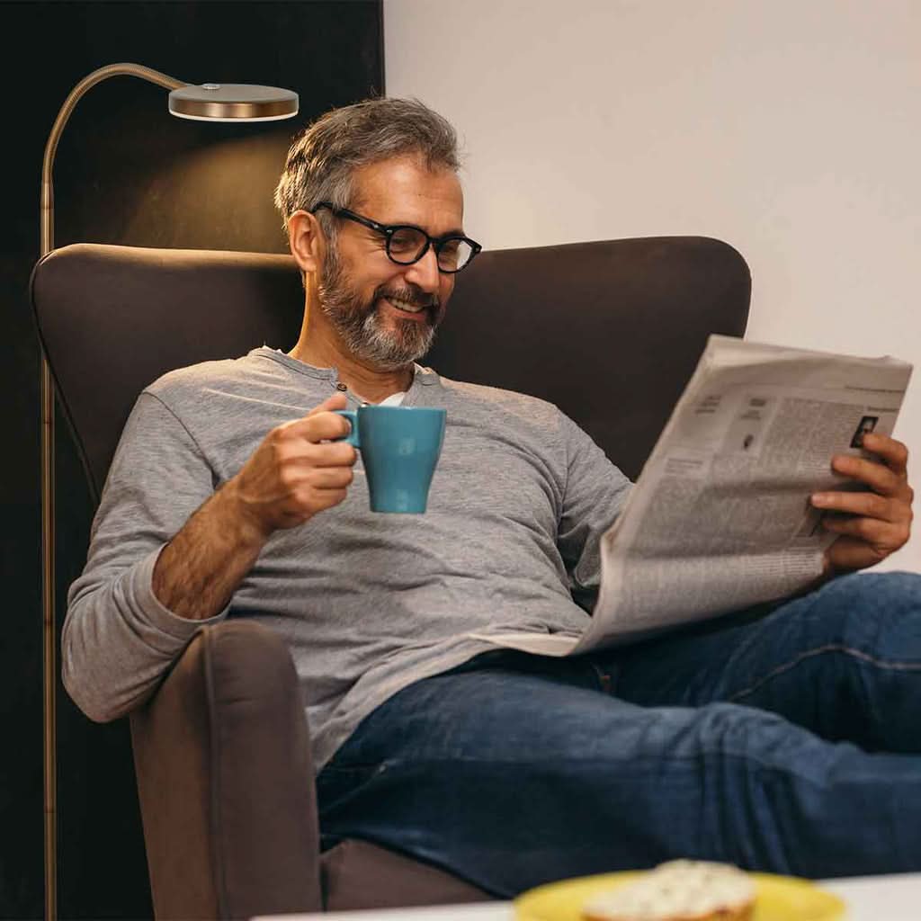 Mise en ambiance : homme lisant son journal, tasse à la main, près du lampadaire