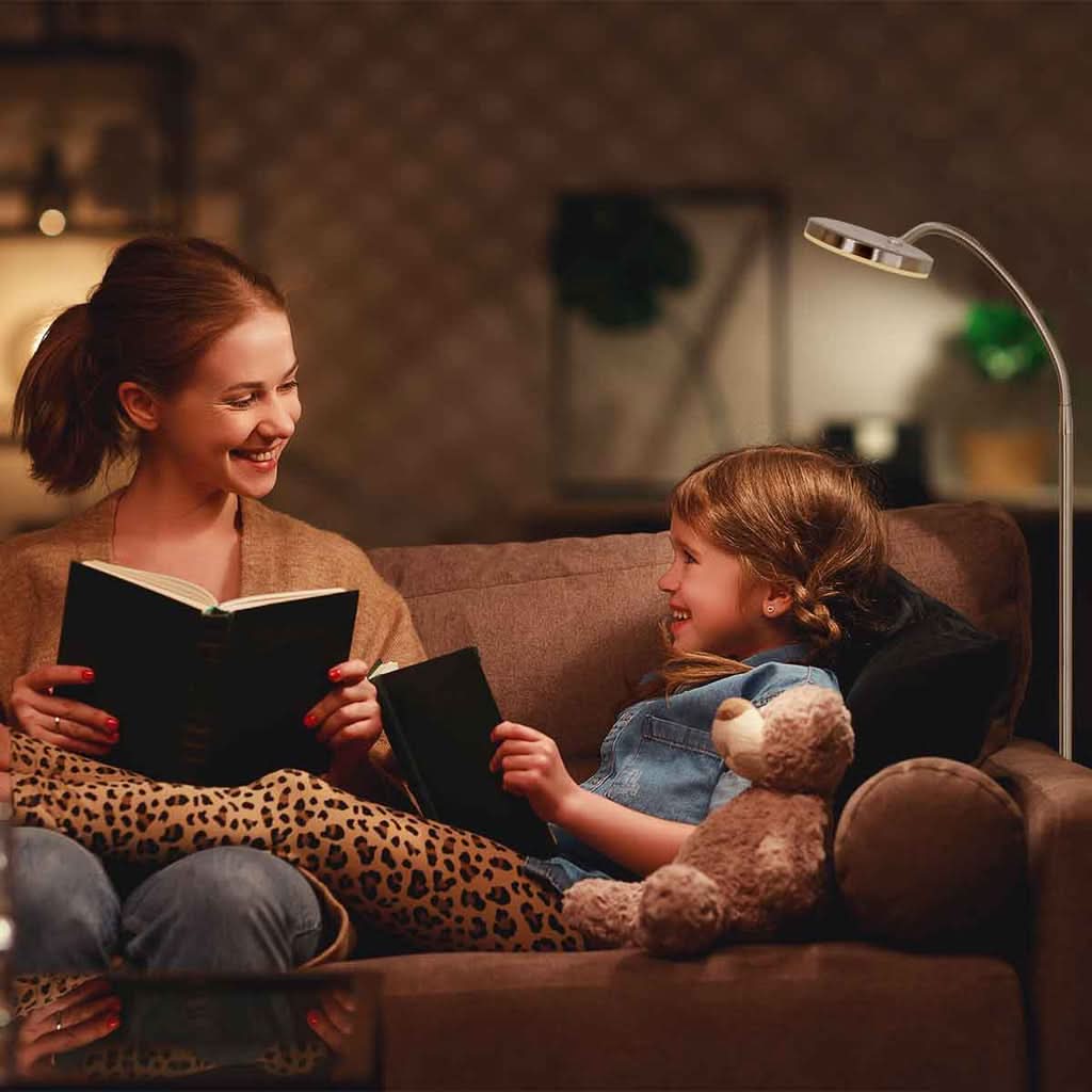 Mise en ambiance chaleureuse, mère et fille lisant sur un canapé éclairées par le lampadaire.