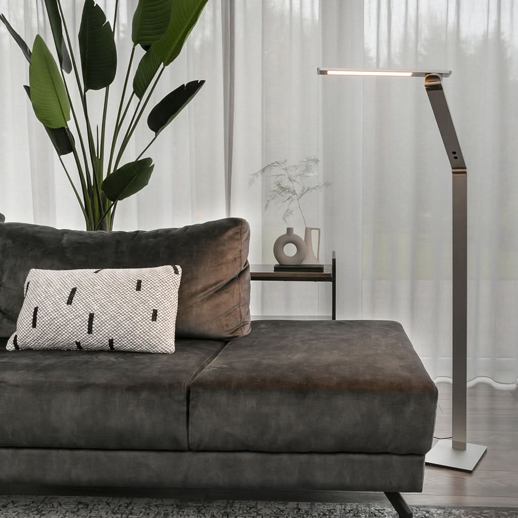 Mise en ambiance salon avec lampadaire allumé près d'un canapé et plante.