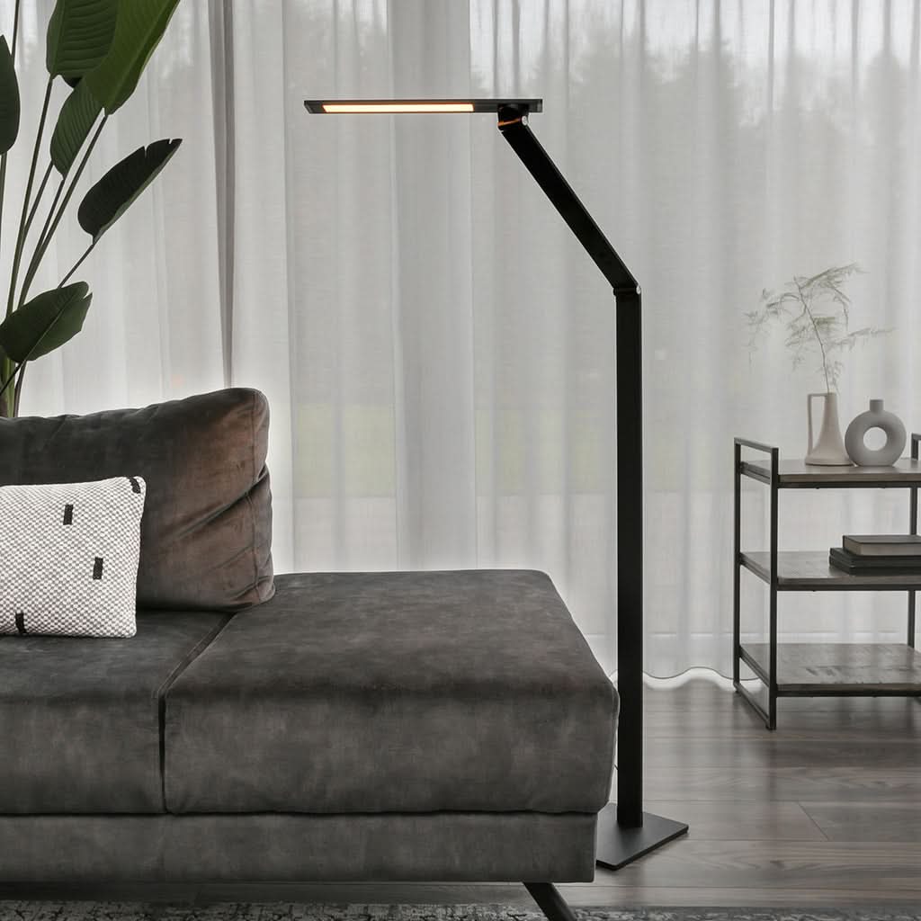 Lampe de sol noire allumée près d'un canapé gris, rideaux transparents en arrière-plan