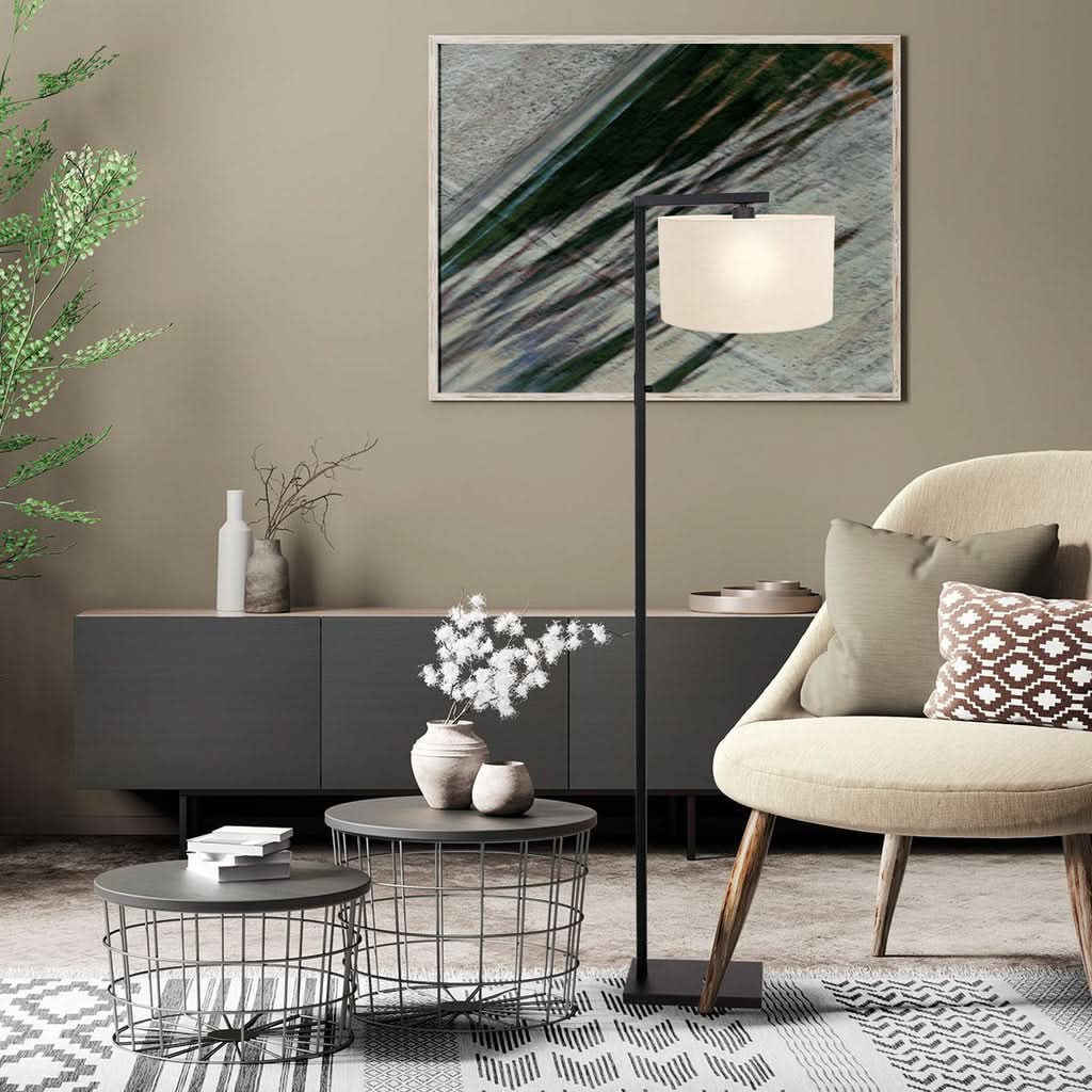 Lampadaire noir allumé avec abat-jour blanc, intégré dans un salon beige et végétal.