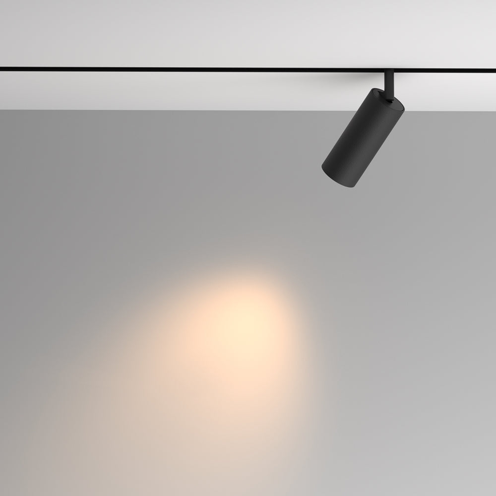 Le spot noir incliné éclaire un mur, fixé sur un rail au plafond.