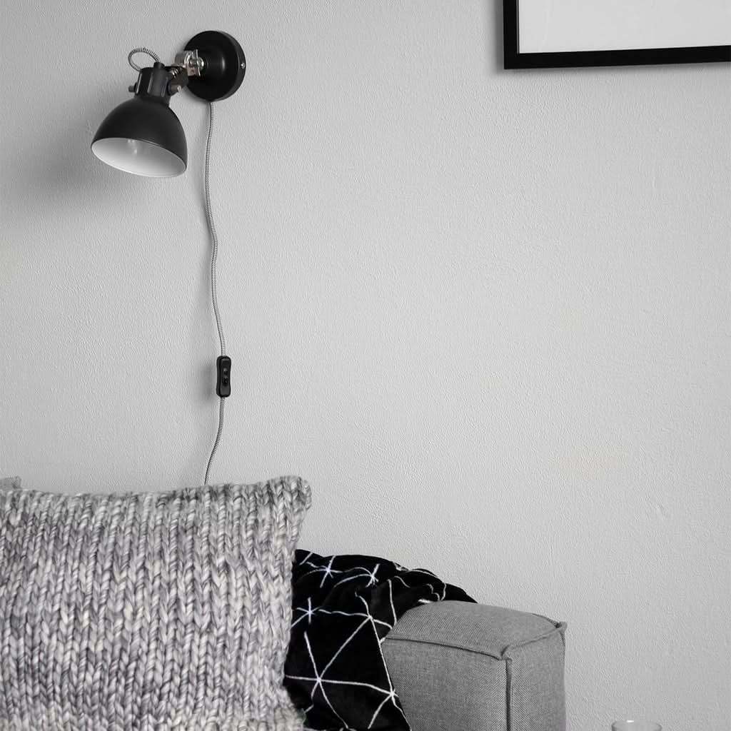 Applique murale noire avec cordon et interrupteur, canapé et coussin en arrière-plan