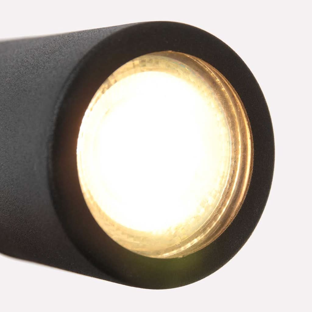 Gros plan de la tête cylindrique allumée, diffuseur en verre et lumière chaude dorée.